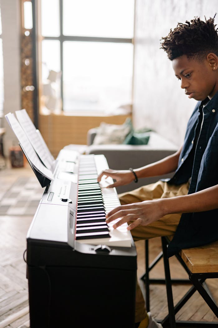 A young man playing the piano in a well-lit room, focused on music.