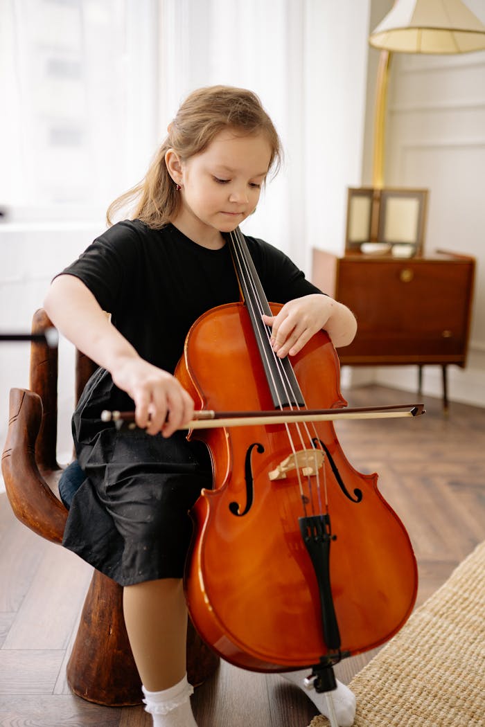 A young girl sitting indoors, skillfully playing a cello, immersed in music.