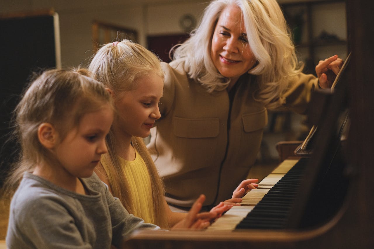 A grandmother joyfully teaches her granddaughters to play piano indoors, fostering musical growth.